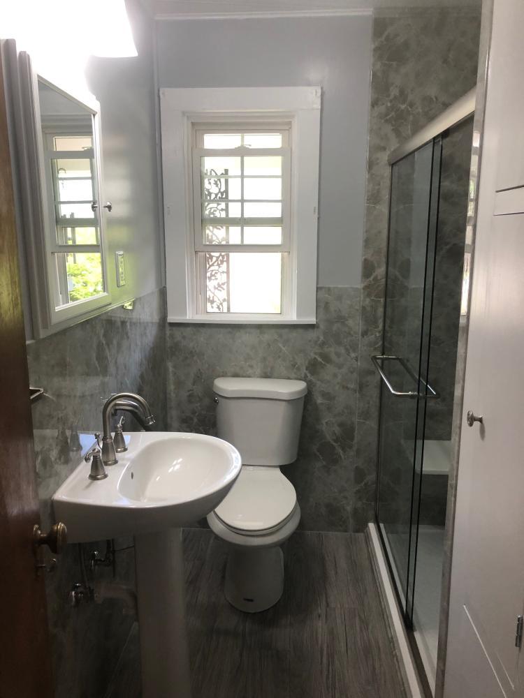 Light Grey Emperador Acrylic not only inside the shower but continues as wainscoting throughout the room. The tub was turned into a low threshold full bench seated shower. Bright white features and accessories compliment the color of walls and grey vinyl plank tile.
