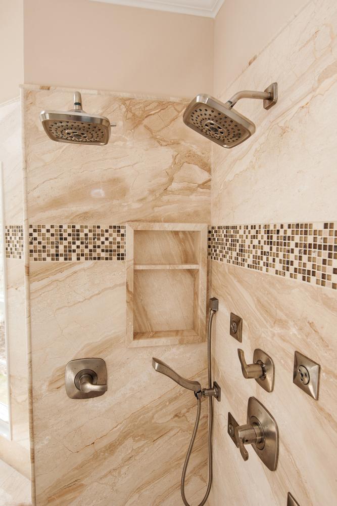 Real natural stone shower with tile mosaic, shelving, and double shower heads.